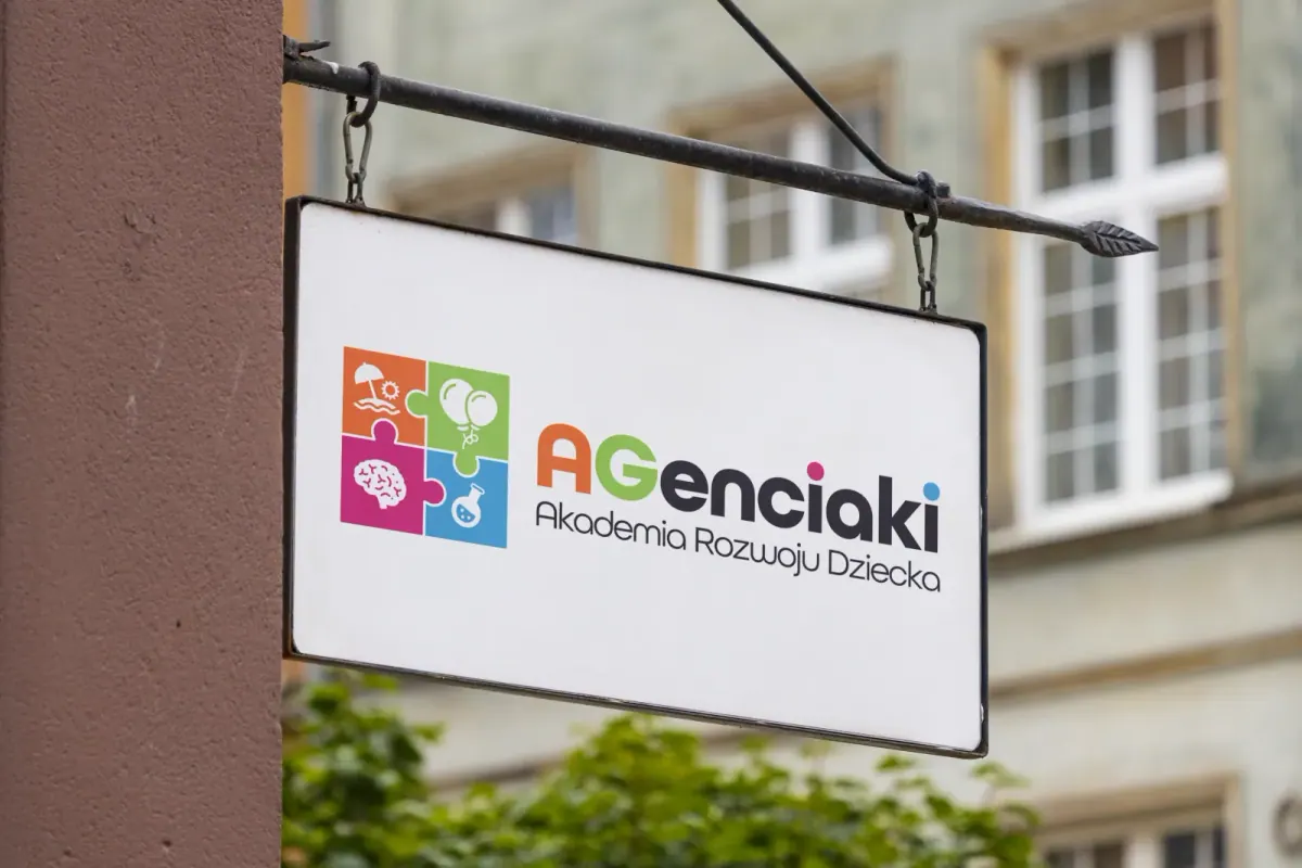Wiszący szyld z kolorowym logo AGenciaki Akademia Rozwoju Dziecka przy okiennej kamienicy
